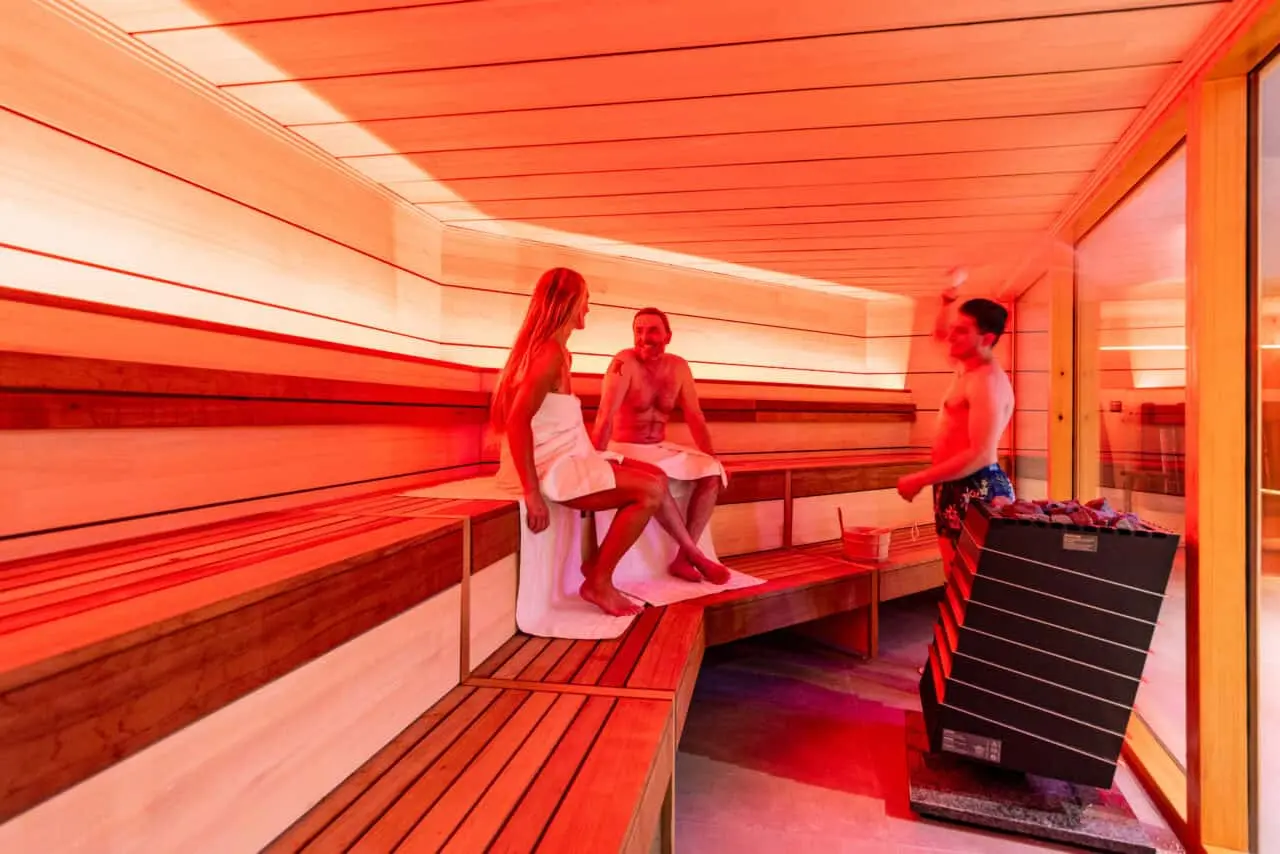 Moderne Sauna mit roter Beleuchtung und Gästen im Wellnessbereich des Best Western Plus Parkhotel Maximilian.