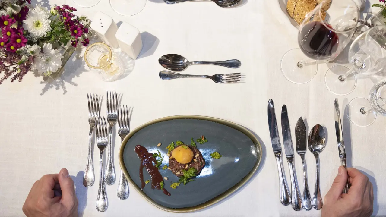 Fein angerichtetes Gericht mit Besteck und Weinglas auf einem elegant gedeckten Tisch im Restaurant des Sporthotel Grandau.