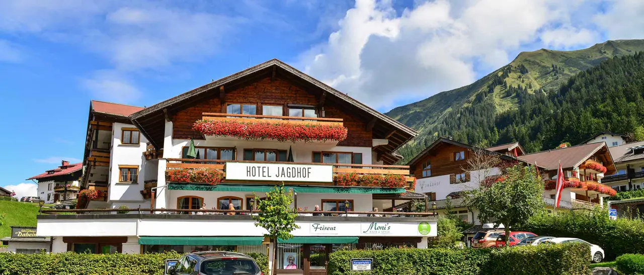 Charmantes Hotel Jagdhof in alpiner Landschaft mit blumenverzierten Balkonen und majestätischem Bergpanorama.