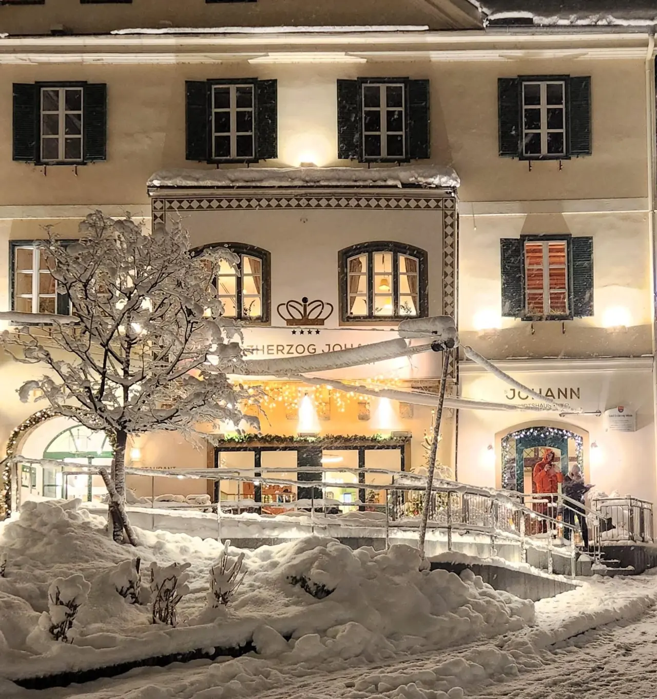 Verschneite Fassade des Spa Hotel Erzherzog Johann bei Nacht, mit warmer Beleuchtung und festlicher Winterdekoration.