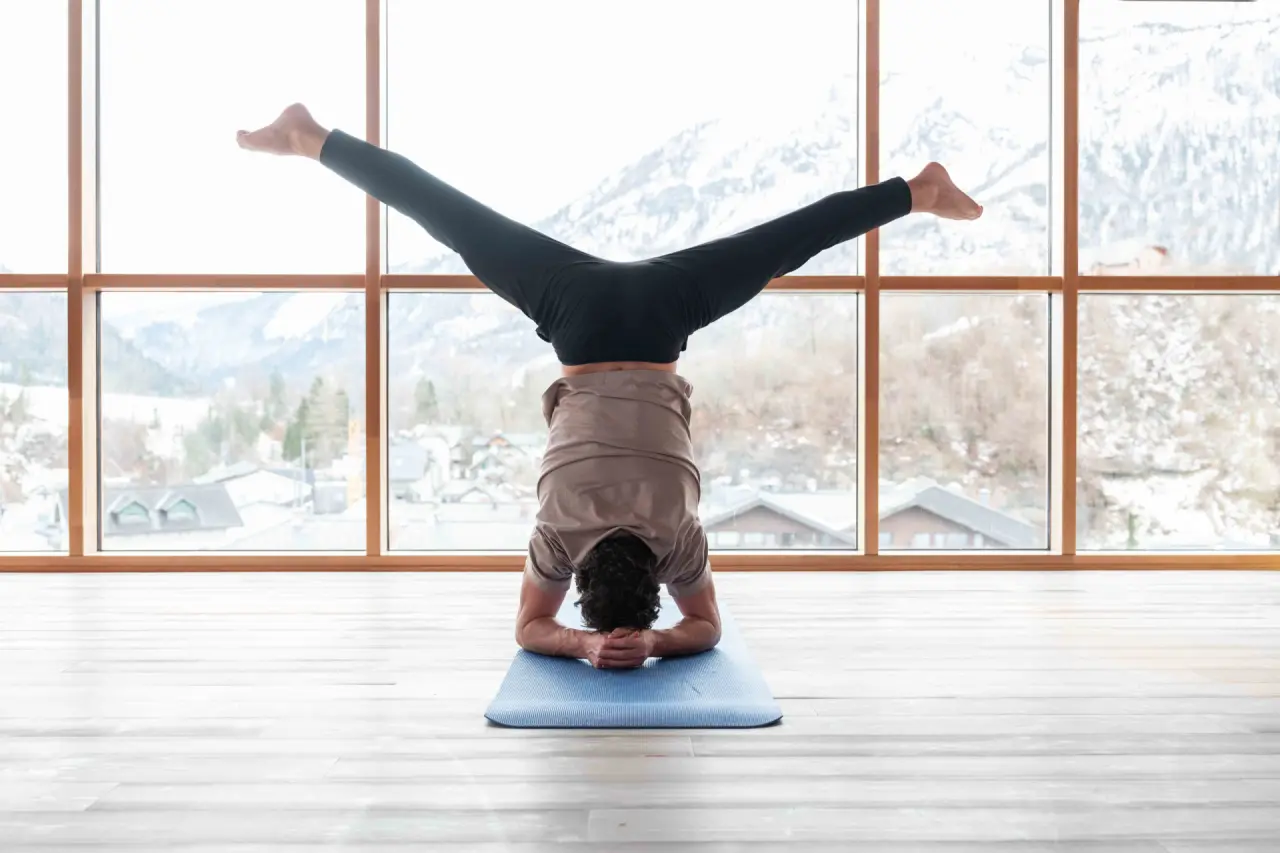 Mann macht Yoga-Kopfstand mit Bergblick im Fitnessraum des Spa Hotel Erzherzog Johann.