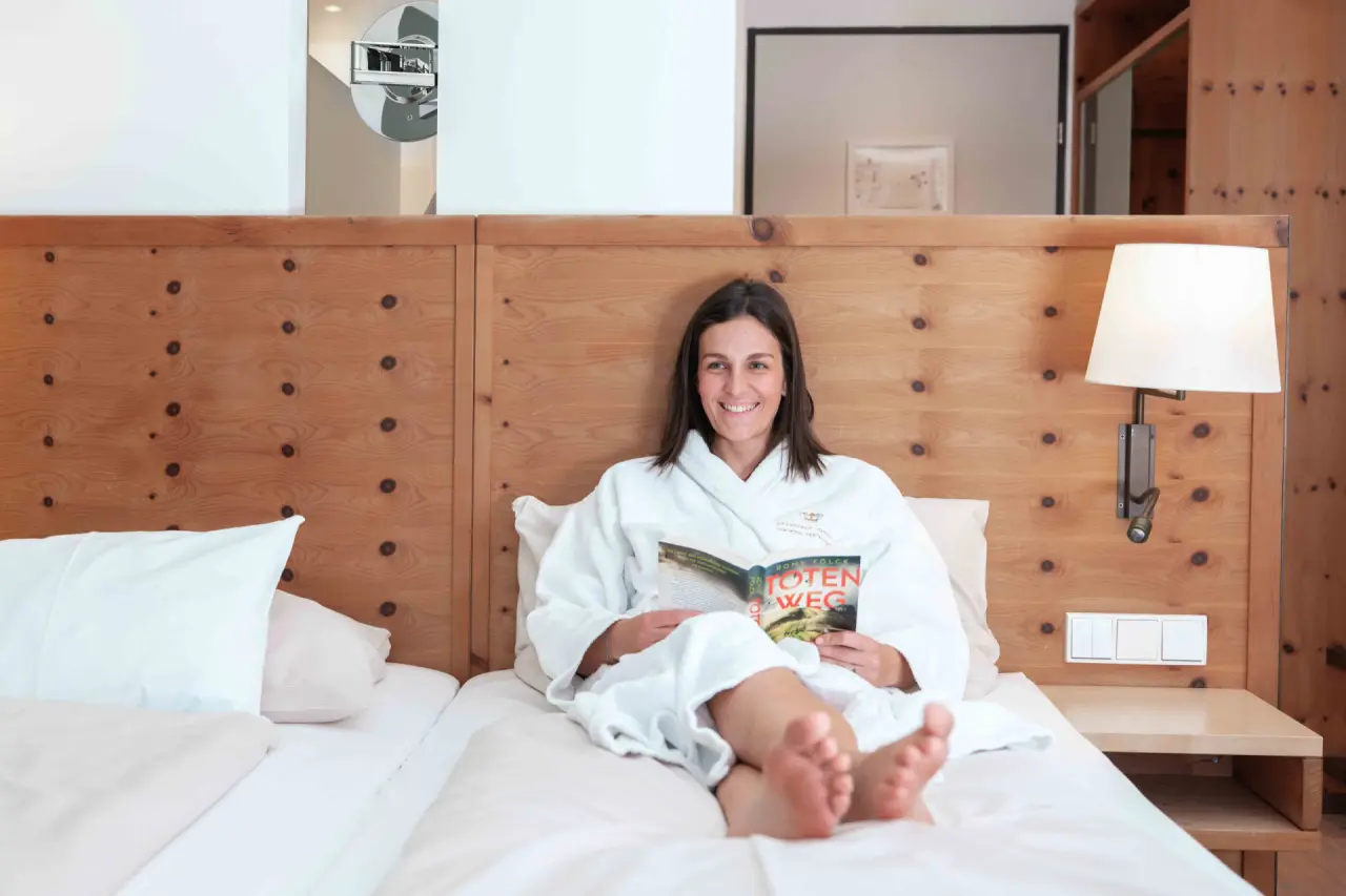 Entspannte Frau im Bademantel liest ein Buch im komfortablen Hotelzimmer des Spa Hotel Erzherzog Johann.