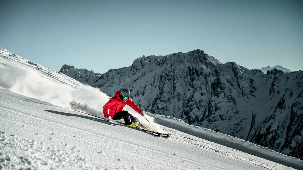 Skifahrer in roter Jacke auf einer Piste mit verschneiten Bergen im Hintergrund, nahe dem Hotel Salnerhof.