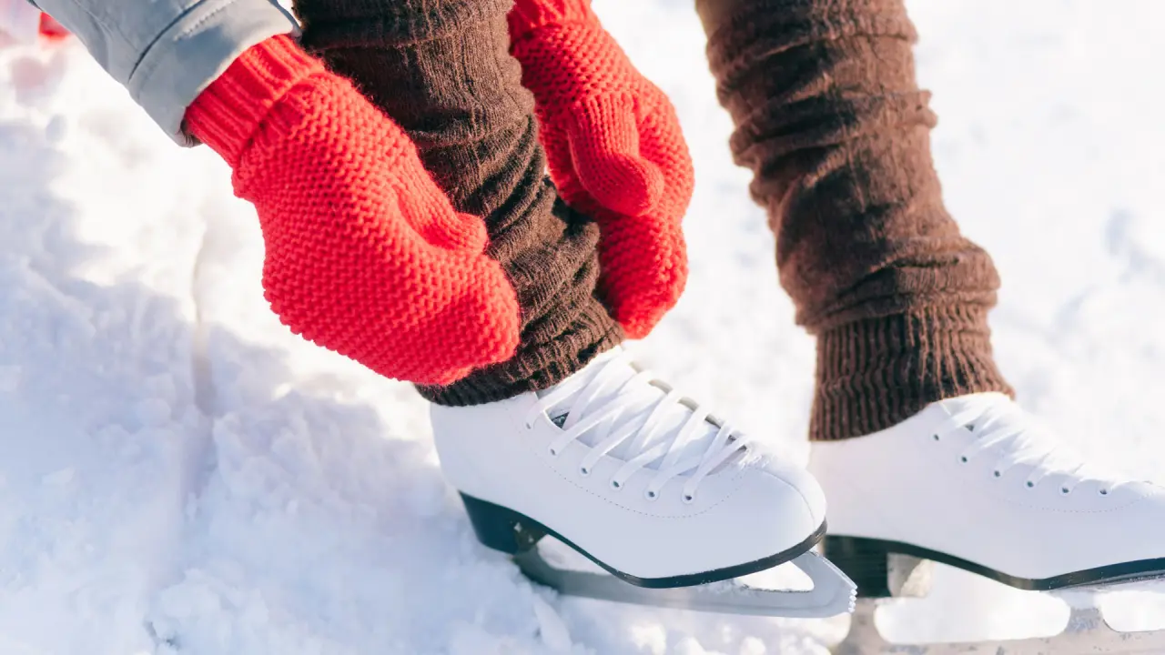 Person schnürt weiße Schlittschuhe mit roten Handschuhen im Schnee, Winteraktivität im Hotel Salnerhof.