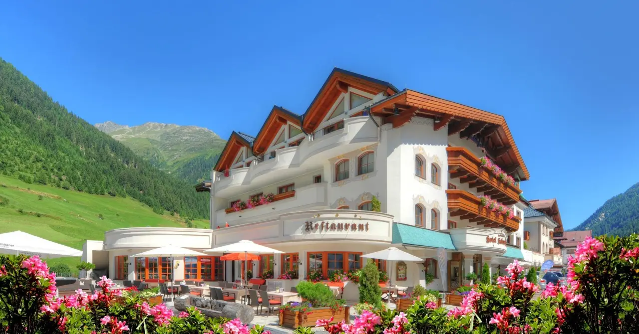 Aussenansicht des Hotel Salnerhof mit traditioneller Architektur, blühendem Garten und Restaurantterrasse vor alpiner Bergkulisse.