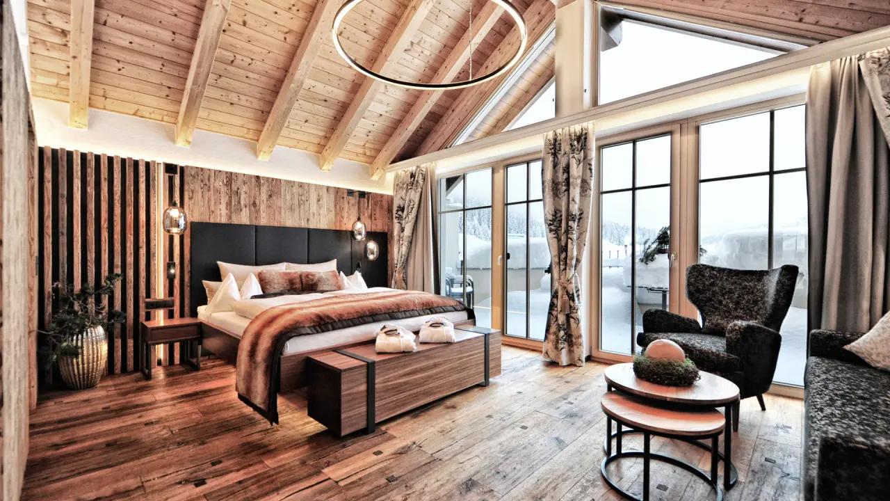 Luxuriöses Hotelzimmer im Hotel Salnerhof mit Holzakzenten, großem Bett und Blick auf die verschneite Winterlandschaft.