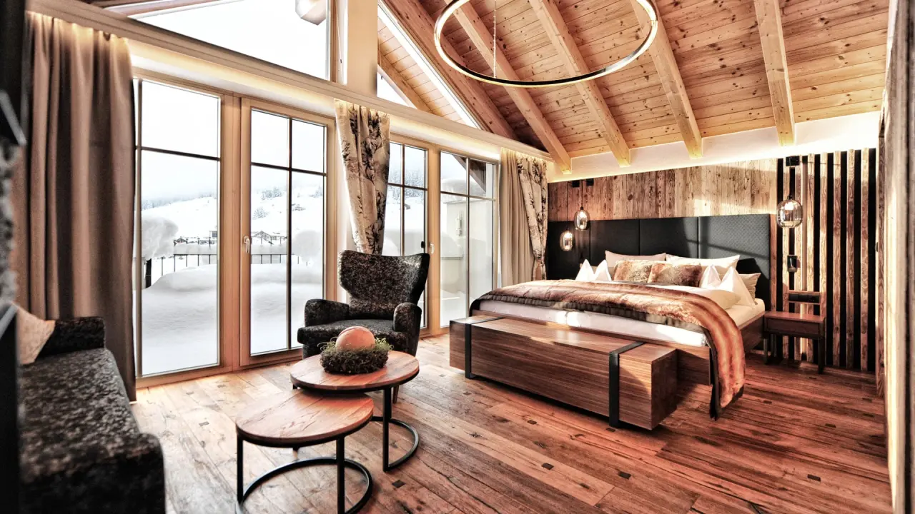 Luxuriöses Hotelzimmer im alpinen Stil mit Holzbalkendecke und Panoramablick auf die verschneite Landschaft im Hotel Salnerhof.