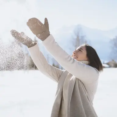 Glückliche Frau spielt mit Schnee in der winterlichen Berglandschaft des LEBE FREI Hotel DER LÖWE.