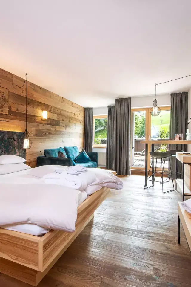 Geräumiges Hotelzimmer mit Holzwand, Doppelbett, Sofa und Balkon im LEBE FREI Hotel DER LÖWE.