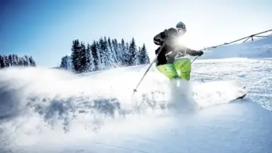 Dynamischer Skifahrer im Tiefschnee mit Sonnenstrahlen und verschneiten Bäumen nahe Hotel Erika.