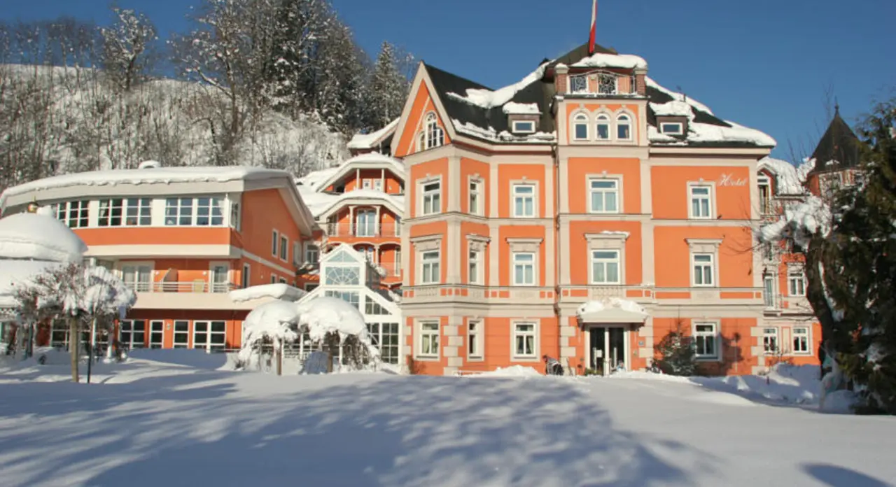 Historisches Hotel Erika in winterlicher Alpenlandschaft mit verschneiter Fassade unter blauem Himmel.
