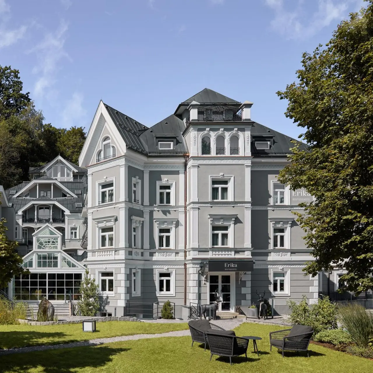 Elegante Aussenansicht des Hotel Erika mit klassischer Architektur, gepflegtem Garten und Sitzgelegenheiten unter blauem Himmel.