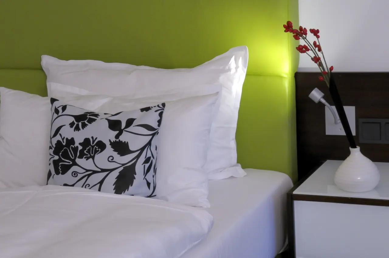 Detailaufnahme eines Hotelzimmers mit grünem Kopfteil, weißen Kissen und Nachttisch im Hotel an der Therme Bad Orb.