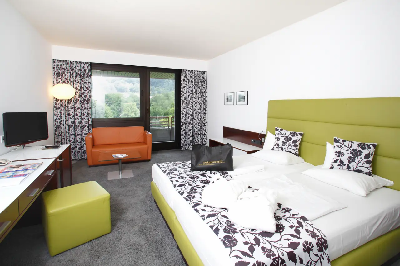 Helles Hotelzimmer im Hotel an der Therme Bad Orb mit Doppelbett, Sitzbereich und Blick ins Grüne.