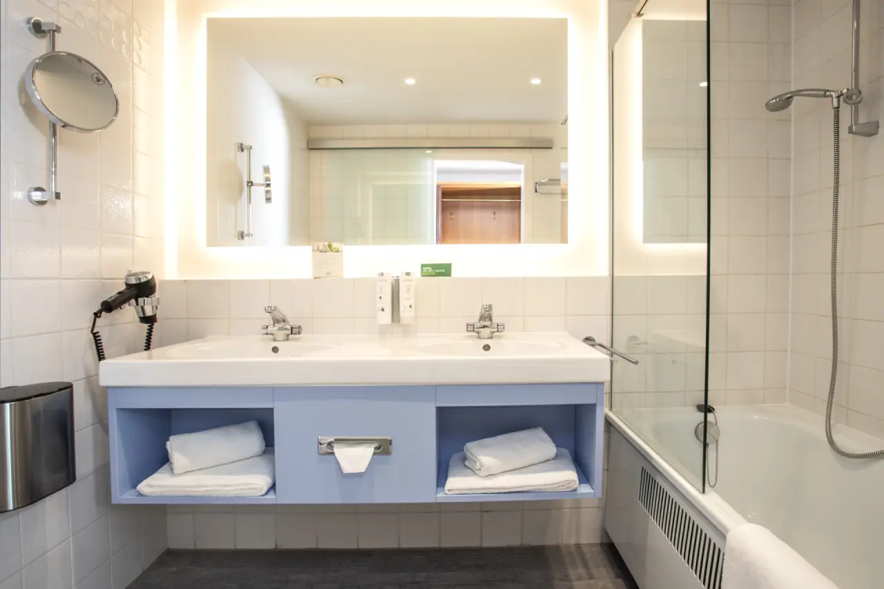 Modernes Badezimmer mit Doppelwaschbecken, beleuchtetem Spiegel und Badewanne im Hotel an der Therme Bad Orb.