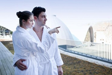 Entspanntes Paar in Bademänteln auf der Sonnenterrasse mit Blick auf die Therme im Hotel an der Therme Bad Orb.