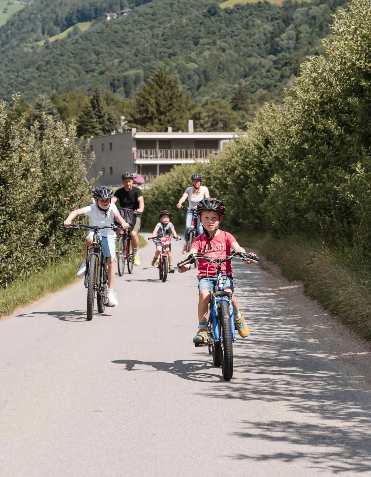 TYROL family retreat in Naturns – Familie beim Radfahren vor der Hotelkulisse | Wellnesshotel Südtirol