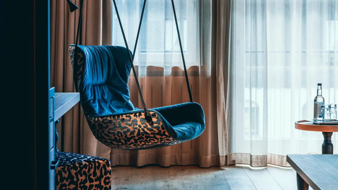 Stilvoller Hängesessel mit Leopardenmuster und blauer Polsterung in einem modernen Hotelzimmer des Hotel Alpenkönig.