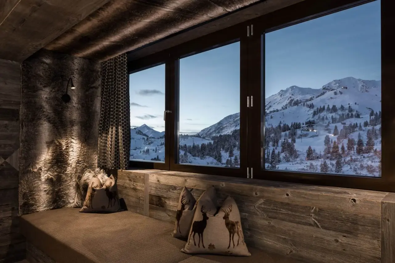 Gemütliche Sitzecke mit Kissen und weitem Blick auf die verschneite Alpenlandschaft im Hotel Das Kohlmayr.