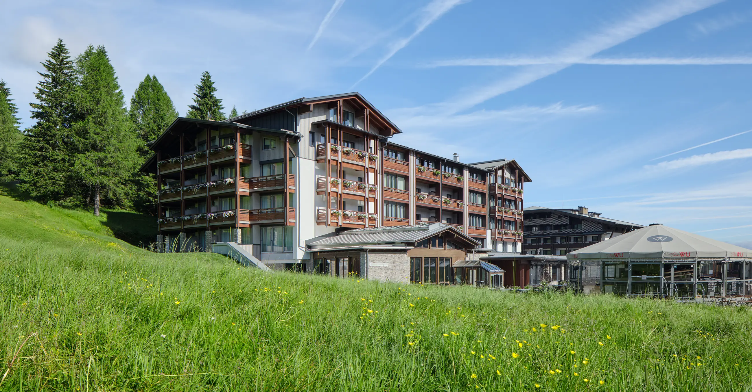 Hotel & Spa Wulfenia in Hermagor – Hotelgebäude im Sommer mit grünen Wiesen | Wellnesshotel Kärnten