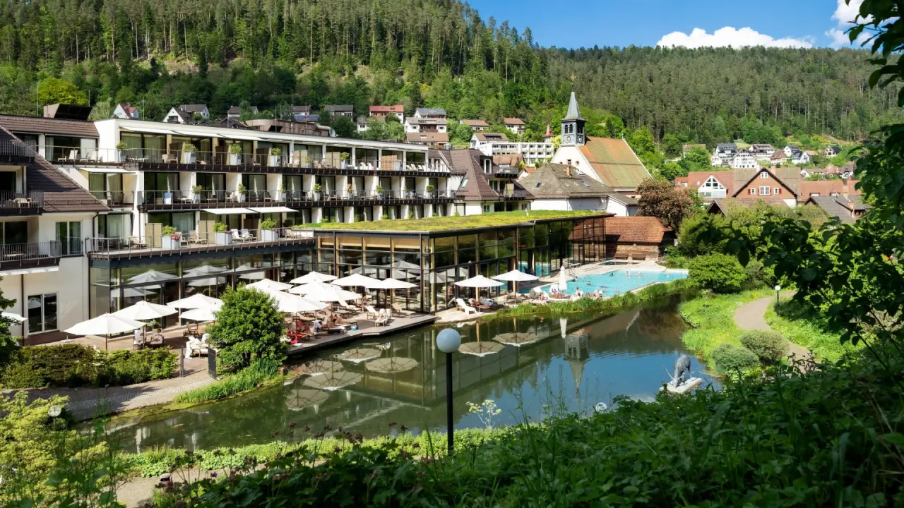 Aussenansicht des Hotel Therme Bad Teinach mit grossem Aussenpool, Sonnenterrasse und umgebender Naturlandschaft.