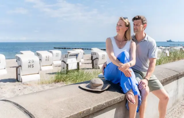 Entspanntes Paar am sonnigen Strand mit Strandkörben und Meerblick, ideal für einen Wellnessurlaub im Ringhotel Strandblick.