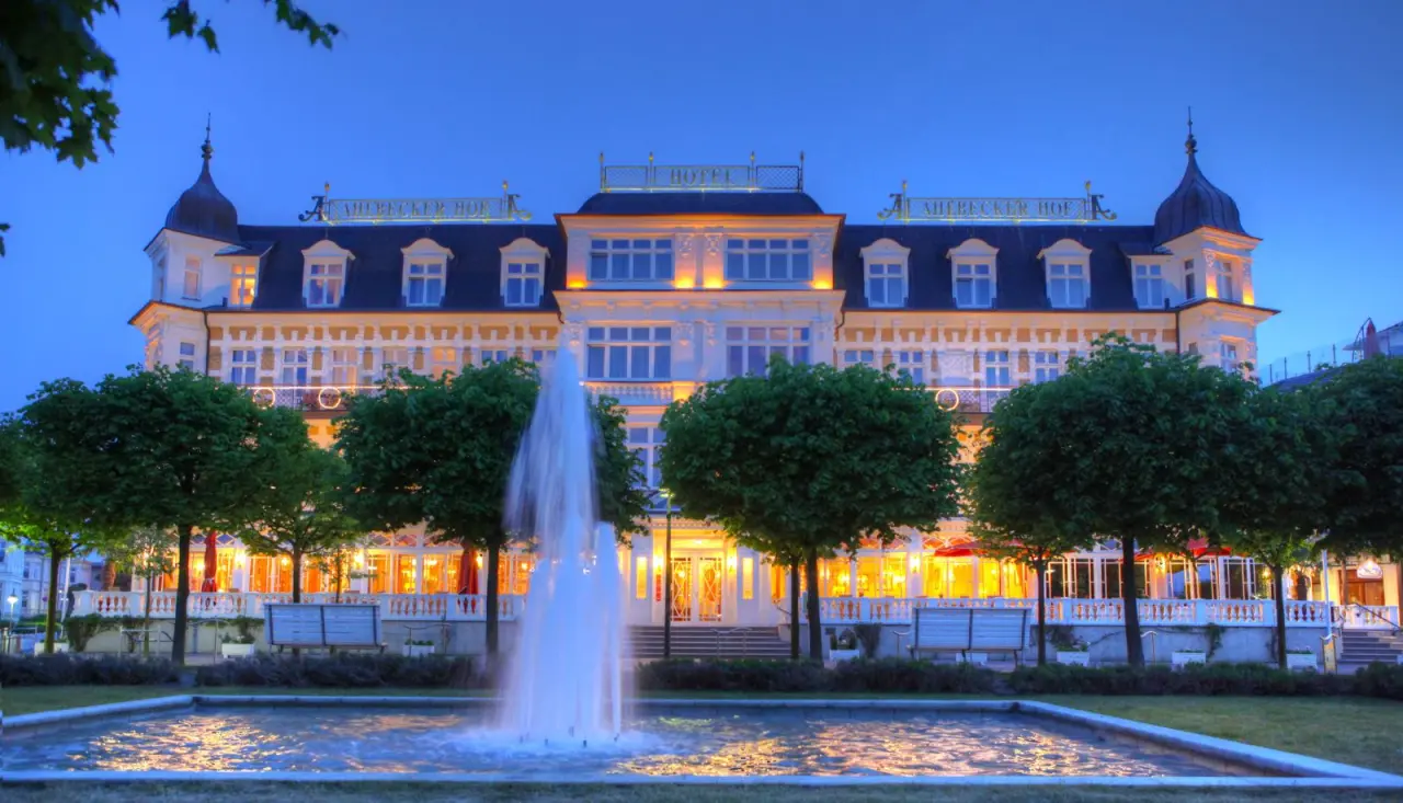 Elegante Aussenansicht des Seetelhotel Ahlbecker Hof bei Dämmerung mit beleuchteter Fassade und Springbrunnen.