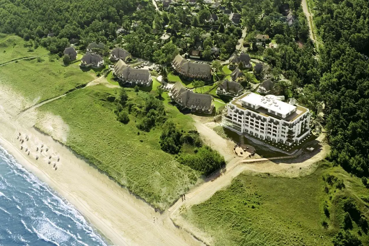Luftaufnahme des Strandhotel Fischland mit modernem Hauptgebäude, Reetdachhäusern, Dünen und direktem Zugang zum Ostseestrand.