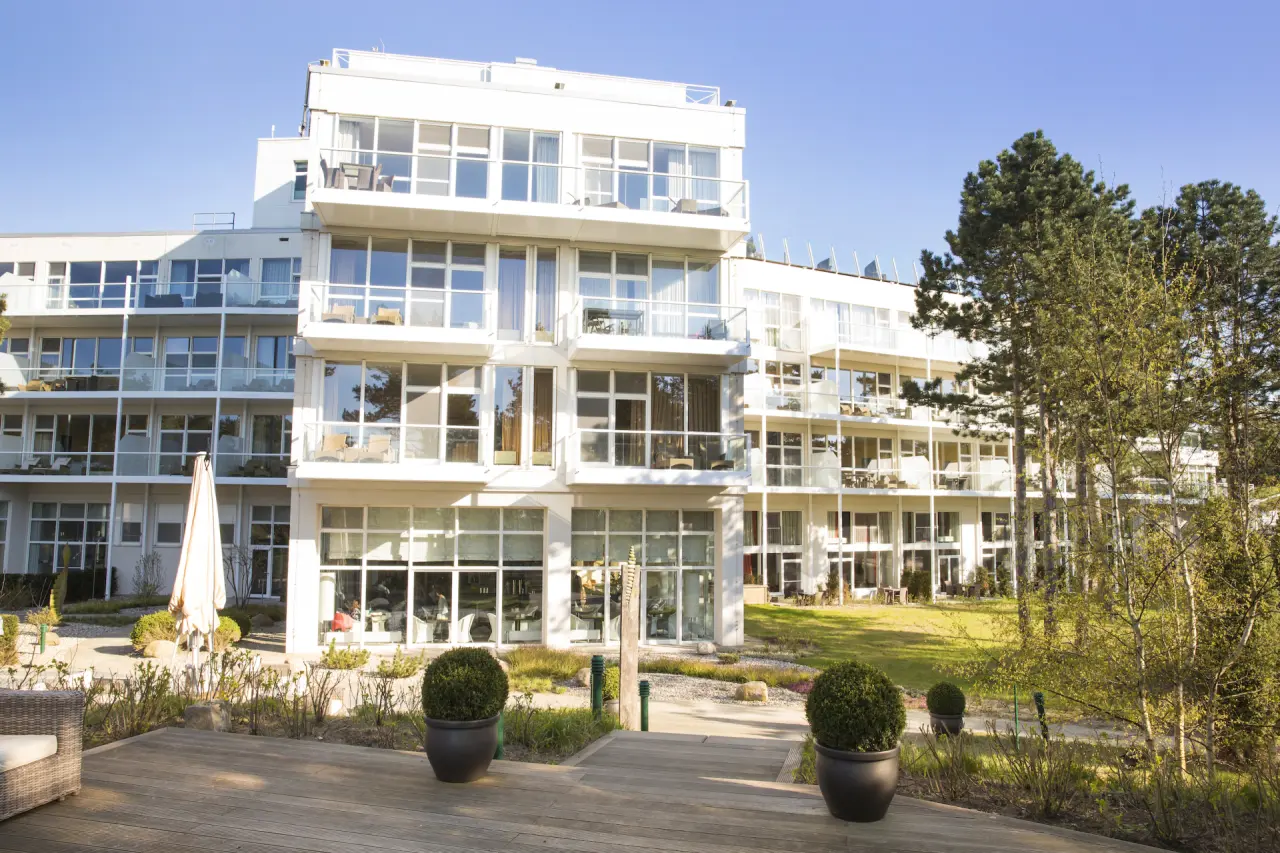 Modernes Strandhotel Fischland mit vielen Balkonen und gepflegter Gartenanlage unter blauem Himmel.