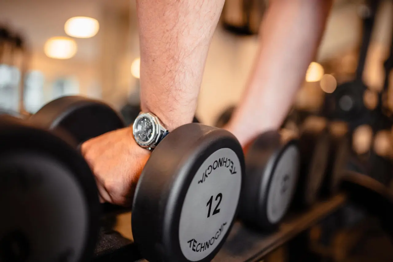 Mann beim Hanteltraining mit 12kg Gewichten im modernen Fitnessbereich des Strandhotel Fischland.
