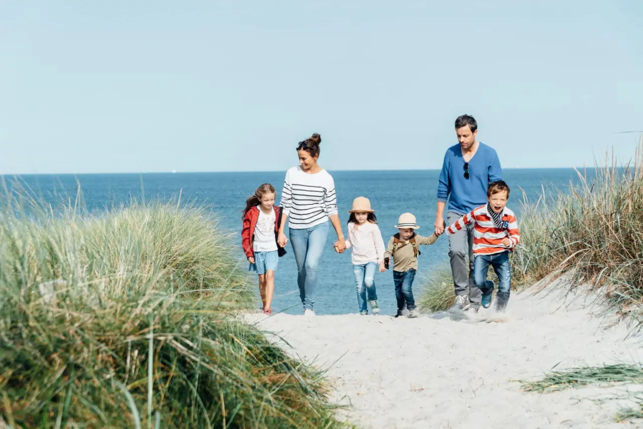 Glückliche Familie spaziert am Sandstrand mit Dünengras und Meer im Hintergrund, ideal für Familienurlaub im Strandhotel Fischland.