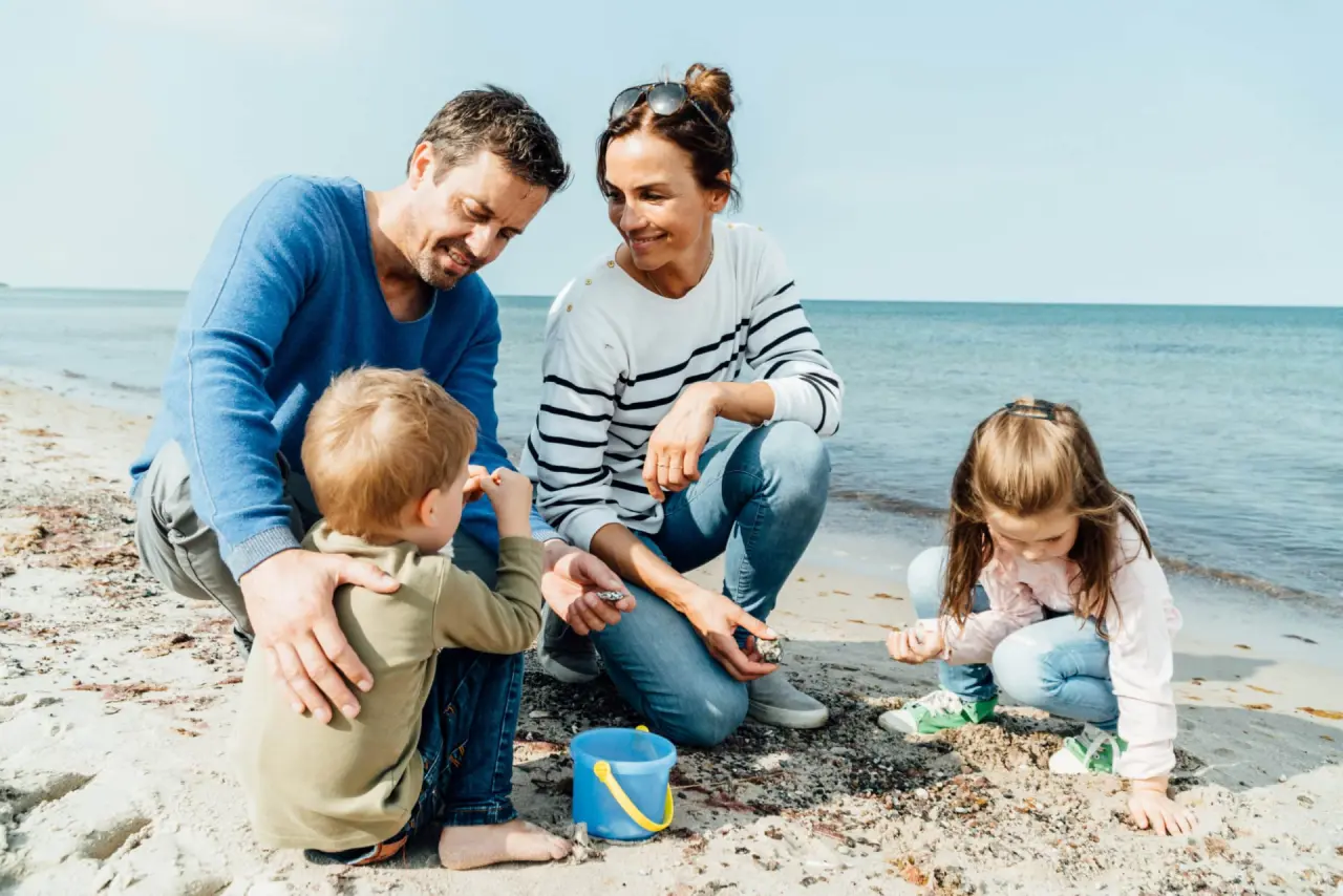 Familie mit Kindern spielt am Sandstrand des Strandhotel Fischland bei strahlendem Sonnenschein und Meerblick.