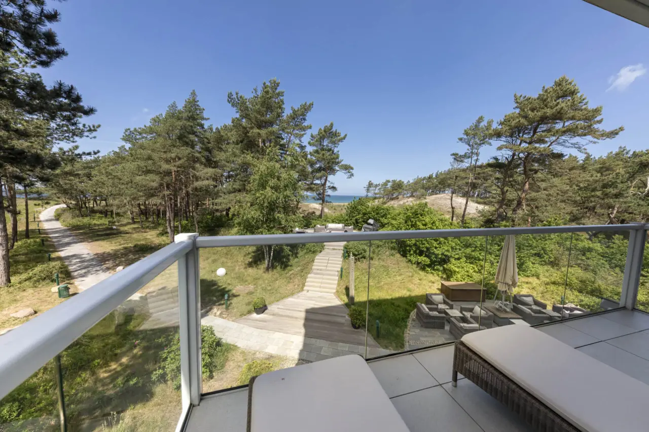 Balkon mit Meerblick und Liegen im Strandhotel Fischland, umgeben von Kiefernwald und Dünenpfad zur Ostsee.