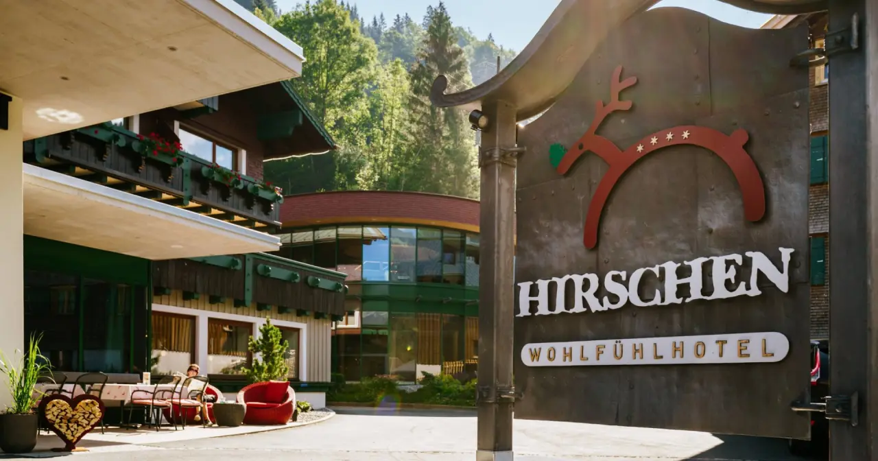 Aussenansicht des Hirschen Wohlfühlhotels mit markantem Hirsch-Logo und einladender Terrasse umgeben von Natur.