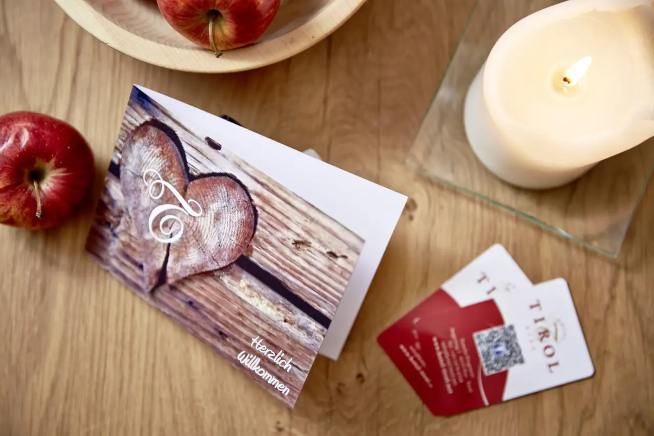 Herzlicher Willkommensgruß im Hotel TIROL mit personalisierter Karte, frischen Äpfeln und brennender Kerze auf Holztisch.