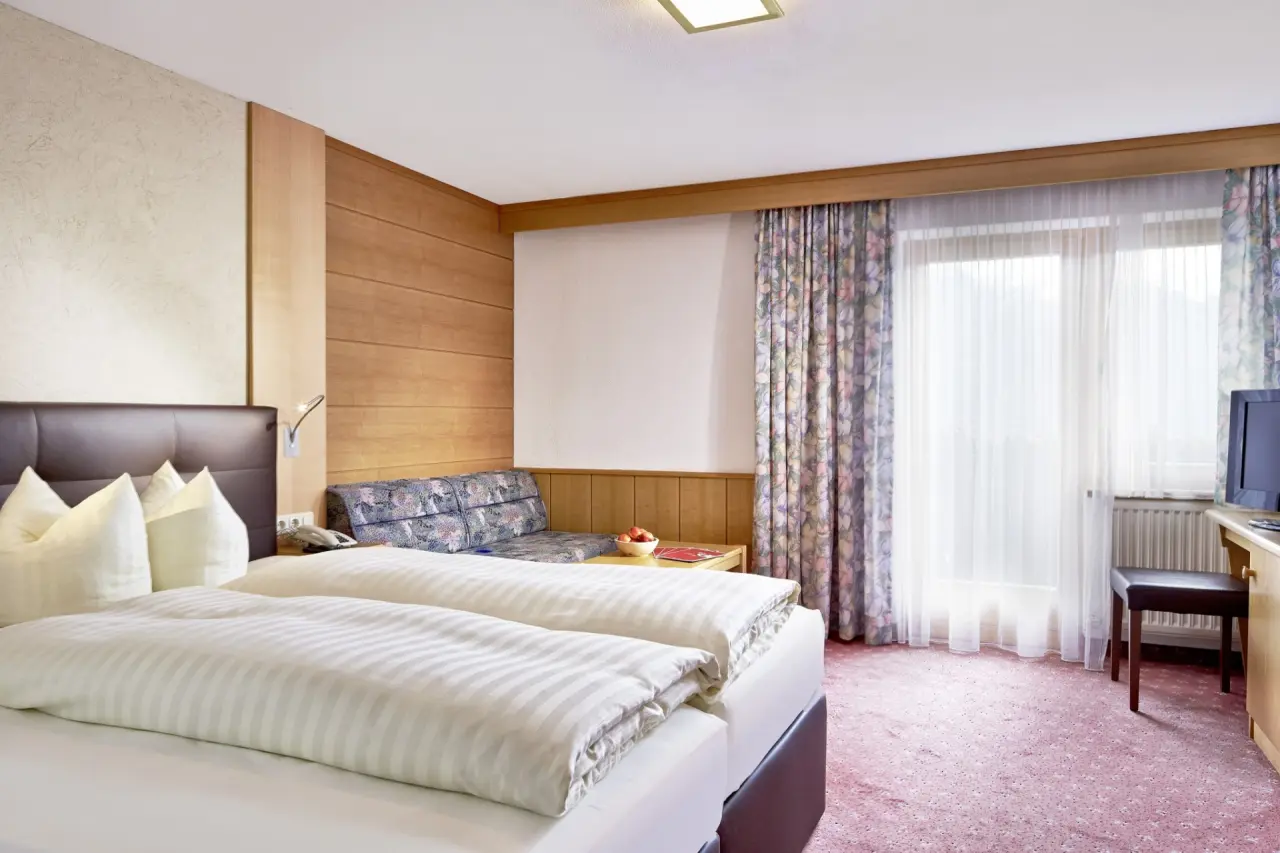 Gemütliches Doppelzimmer im Hotel TIROL mit bequemen Betten, kleinem Sitzbereich und Fenster mit Vorhängen.