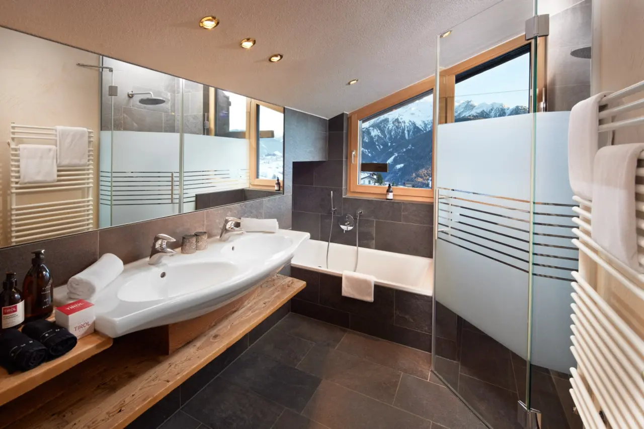 Modernes Badezimmer im Hotel TIROL mit Badewanne, Dusche und Bergblick auf die verschneiten Alpen.