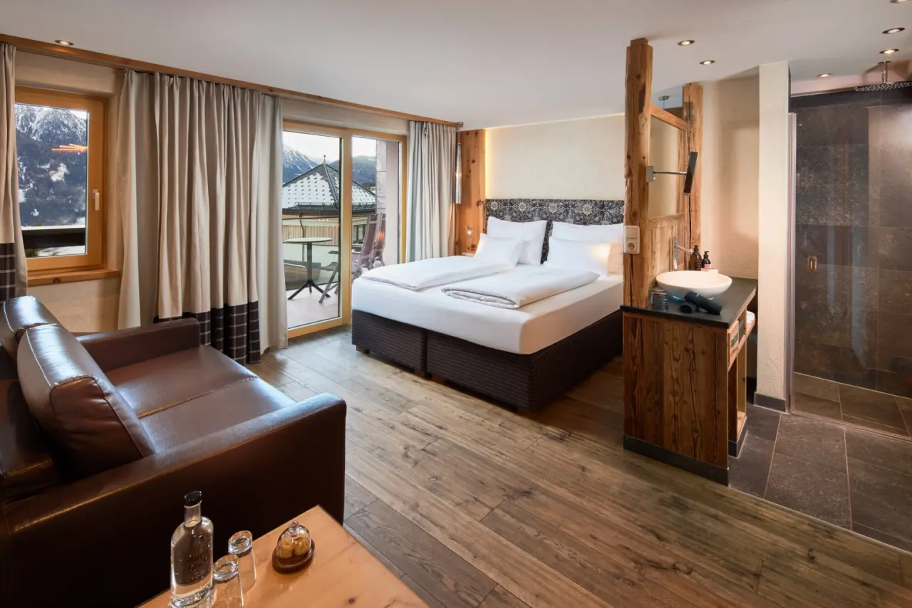 Geräumiges Doppelzimmer im Hotel TIROL mit gemütlichem Sofa, offenem Bad und Balkon mit Bergblick.