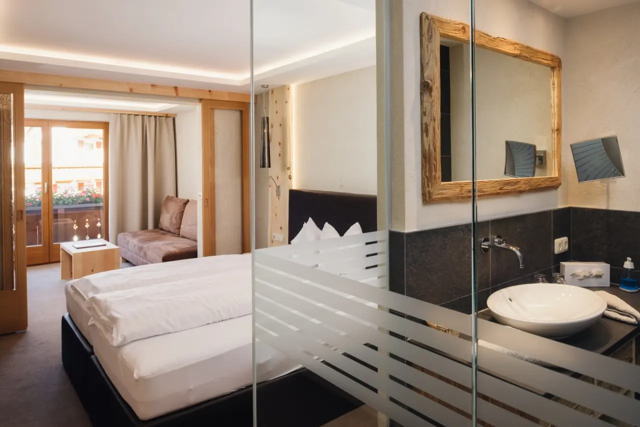 Gemütliches Hotelzimmer im Hotel TIROL mit Doppelbett, Sofa, Balkon und integriertem Badbereich mit Holzspiegel.