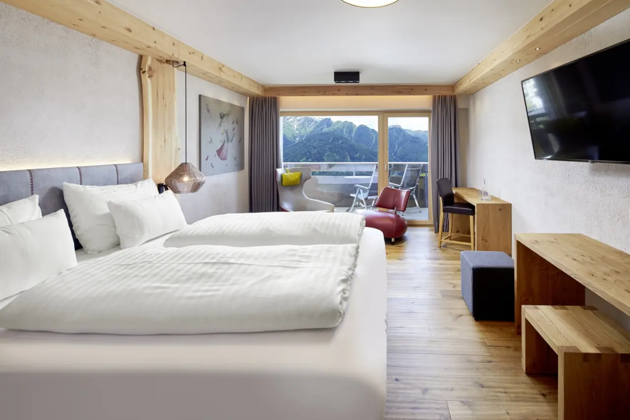 Geräumiges Hotelzimmer im Hotel TIROL mit Doppelbett, Holzelementen und Balkon mit atemberaubendem Bergblick.