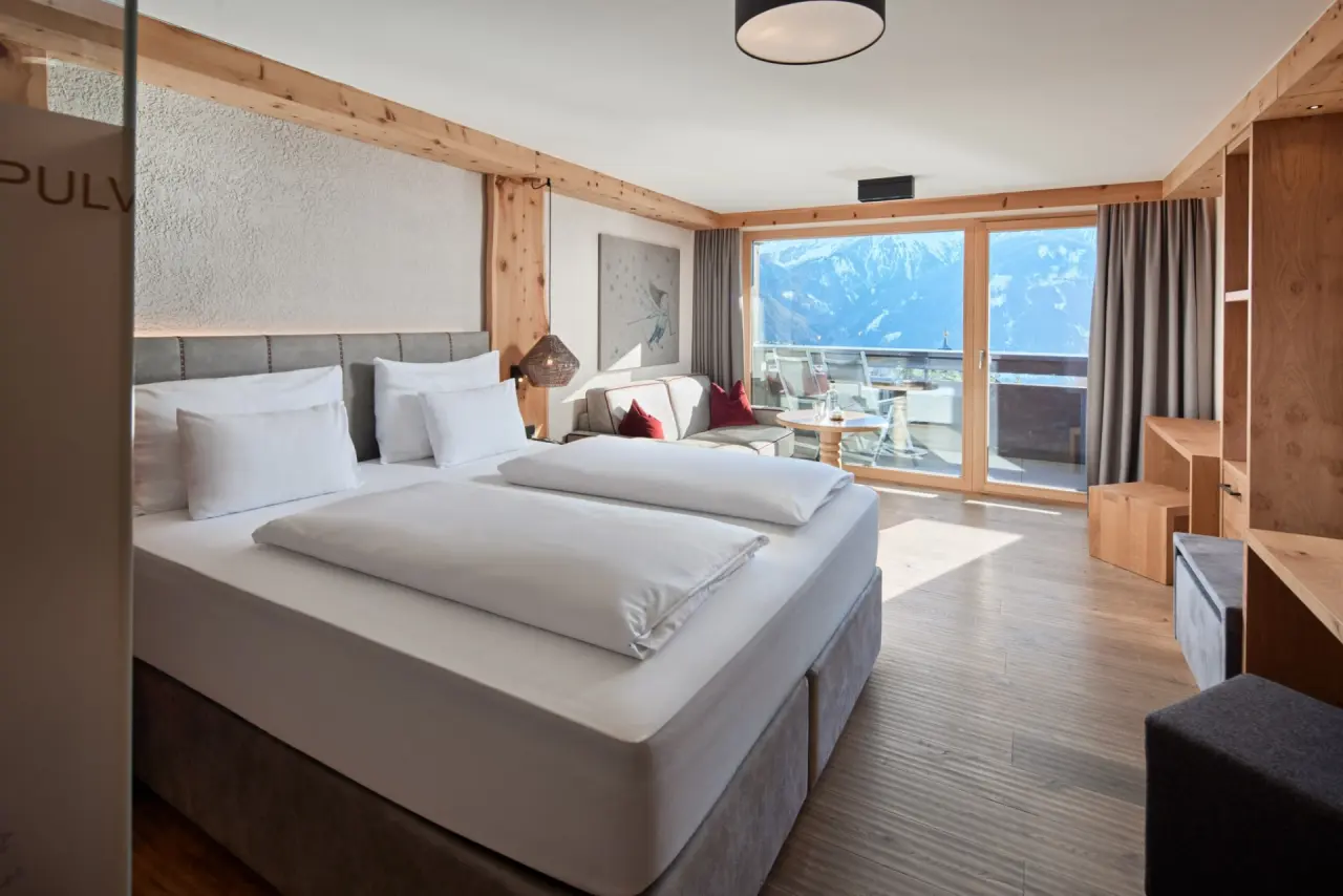 Geräumiges Hotelzimmer im Hotel TIROL mit Doppelbett, Sitzbereich und Balkon mit atemberaubendem Bergblick.