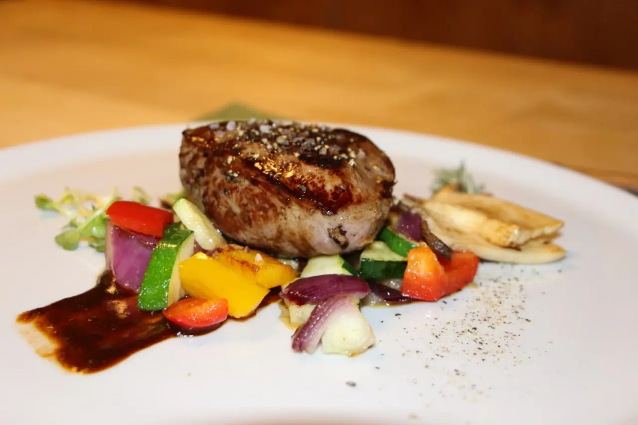 Ansprechend angerichtetes Rinderfilet mit frischem Gemüse und Sauce auf einem weißen Teller im Hotel Berghof.