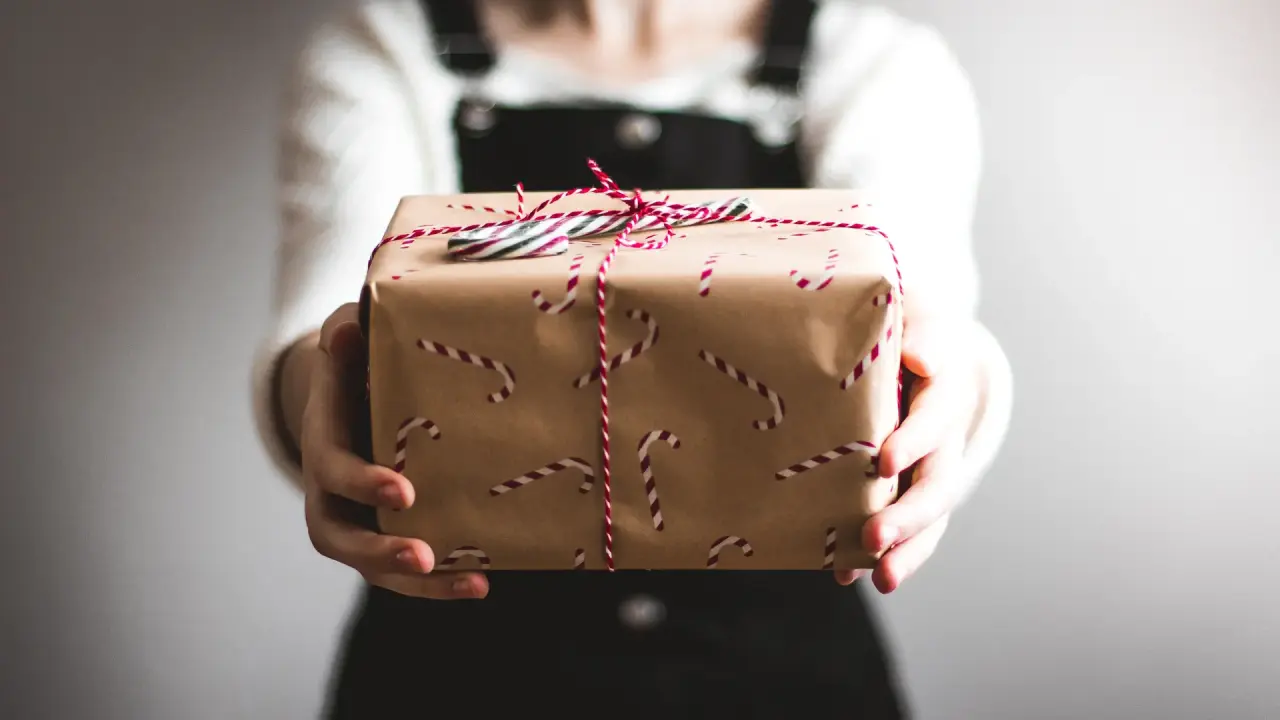 Person hält ein braunes Geschenkpaket mit roten Zuckerstangen und Schnur. Ideal für Gutscheine des Fritz Lauterbad Wellnesshotels.