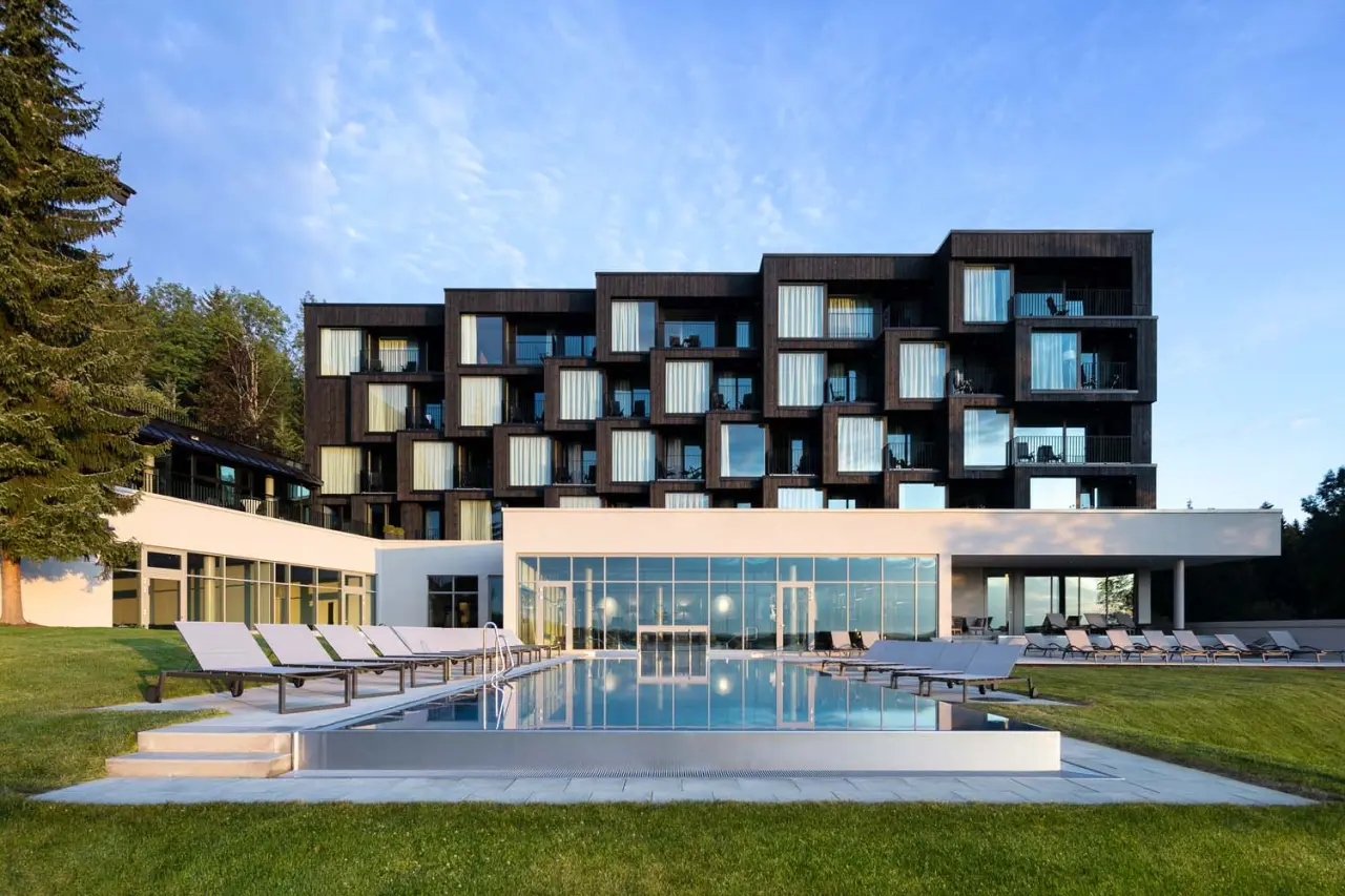 Modernes Wellnesshotel Fritz Lauterbad mit Aussenpool und Liegewiese vor Waldkulisse unter blauem Himmel.
