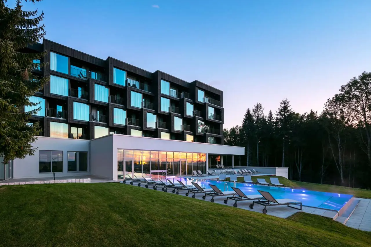 Modernes Wellnesshotel Fritz Lauterbad mit beleuchtetem Aussenpool und Liegen im Abendlicht, umgeben von Natur.