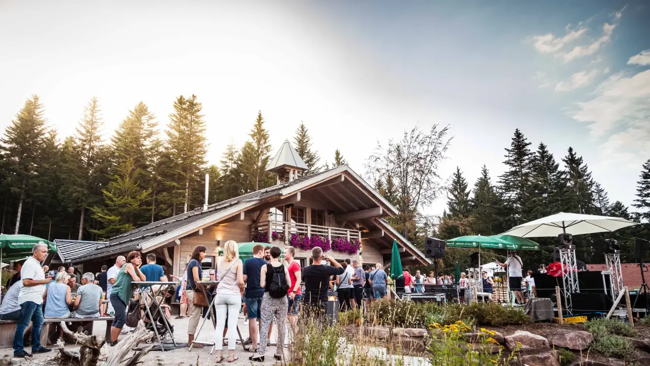 Belebtes Outdoor-Event mit Gästen vor dem traditionellen Holzhaus im Garten des Fritz Lauterbad Wellnesshotels.