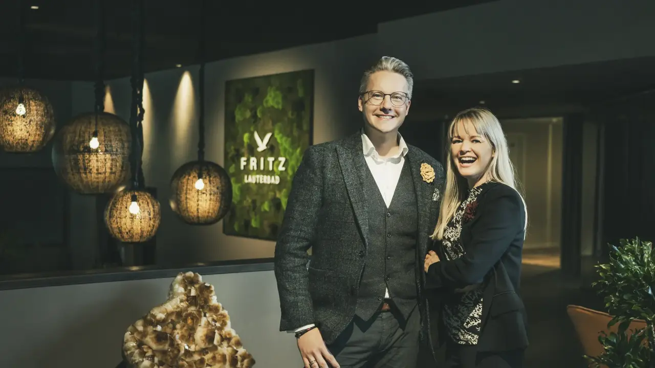 Die Gastgeber des Fritz Lauterbad Wellnesshotels lächeln in der stilvollen Lobby mit Mooswand und Designleuchten.