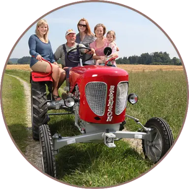 Familie auf rotem Oldtimer-Traktor auf einem Feldweg beim Landhotel Moorhof.