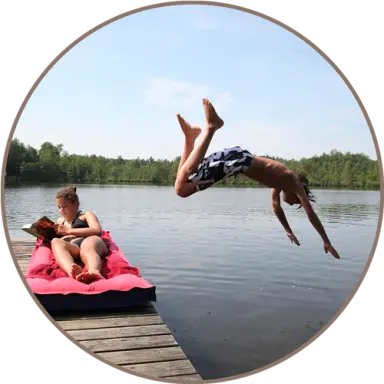 Sommerlicher Badespaß am Natursee des Landhotel Moorhof mit springendem Jungen und entspanntem Mädchen am Steg.