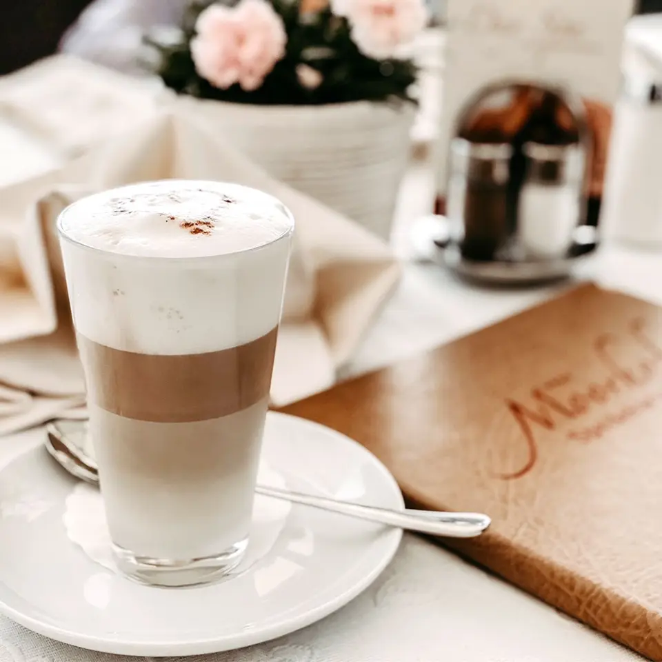 Latte Macchiato im Restaurant des Landhotel Moorhof mit Speisekarte und Blumen auf dem Tisch.